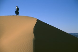 LIBYA, Sahara Desert, Tuareg man standing on ridge of sand dune.