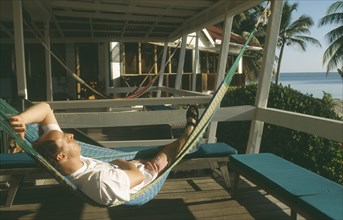 BELIZE, Placencia, Man relaxing in hammock at the Rum Point Inn