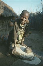 UGANDA, Karamoja, Tribal Poeple, Dodoth Karamojong girl grinding millet on stone.