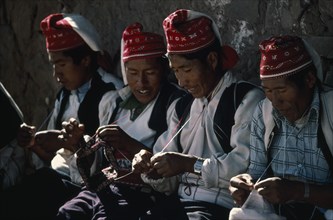 PERU, Puno, Lake Titicaca, Taquile Island.  Line of men knitting.
