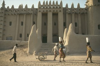 MALI, Djenne, Exterior of mud brick mosque built in traditional style with woman walking past