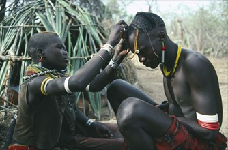 UGANDA, Karamoja, Tribal Peoples, Karamojong warrior having beaded head dress fixed by a friend.