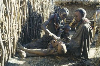 UGANDA, Karamoja, Female witch doctor or Amuron using sysal to suck out evil from child affected by