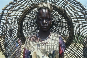 SUDAN, Bahr el Ghazal, Portrait of young Dinka woman with fishing basket behind her casting shadow