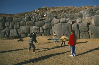 PERU, Cusco, Sacsayhuaman, Local children playing volleyball in front of walls of Inca fort on