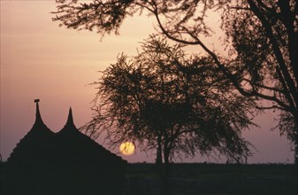 SUDAN, South, Dinka huts silhouetted at sunset.