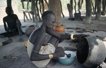 SUDAN, Tribal People, Young Dinka woman ladelling the oil produced from shea butter fruit after