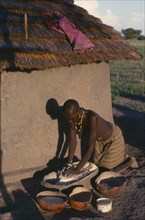 SUDAN, Tribal People, Dinka woman grinding dura outside hut casting shadow on wall.