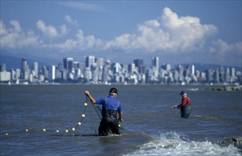 CANADA, British Columbia, Vancouver, English Bay.  Fishermen with net in foreground and skyline of