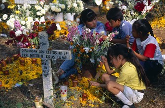 MEXICO, Michoacan, Patzcuaro, Tzurumutaro Cemetery.  Woman and children making graveside vigil as