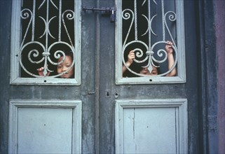 VIETNAM, North, Hanoi, Children looking out from behind decorative ironwork door panels of house in