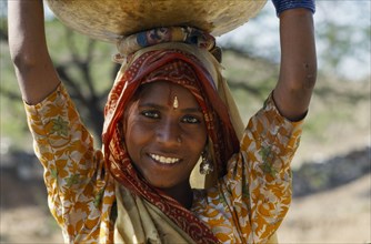 INDIA, Rajasthan, Jodhpur, Smiling girl carrying a water vessel on her head.