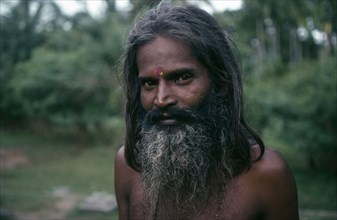 SRI LANKA, People, Men, Portrait of man with beard and long hair standing within green landscape.