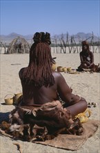 NAMIBIA, Skeleton Coast, Hoarusib Valley, Kaokoland.  Back of seated Himba woman wearing calfskins