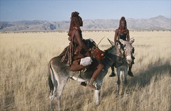 NAMIBIA, Marienfluss, Himba women and child on donkeys in grassland area.