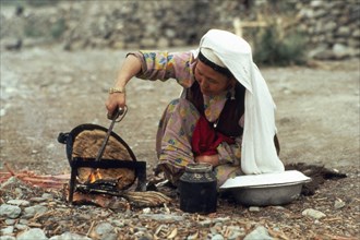 AFGHANISTAN, Tribal People, Kirghiz woman baking bread on outside fire.