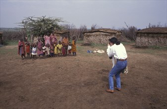 KENYA, , A Japanese tourist photographs a maasai family in a cultural manyatta set up to interface