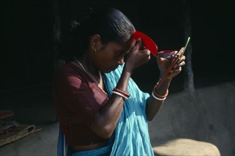 INDIA, Religion, Hinduism, Young woman applying red sindoor paste to central parting of hair to
