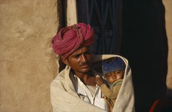 INDIA, Rajasthan, People, Man holding child wrapped in shawl on cold morning.