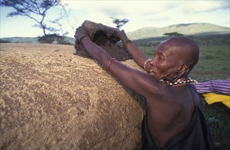 KENYA, Kajiado, A Maasai woman covers her hut with cow dung which has the effect of waterproofing