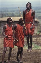 KENYA, Kajiado, Maasai Moran measure each others capacity to jump springing from a standing start.