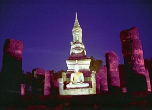 THAILAND, Sukhothai, Seated stone Buddha illuminated at dusk with surrounding columns