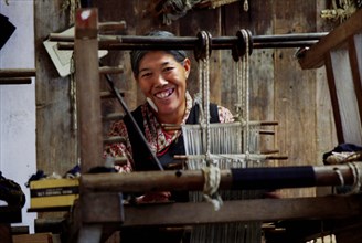 INDIA, Sikkim, Rumtek, Smiling Tibetan lady weaving fabric on a loom