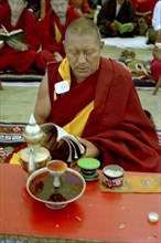 INDIA, Ladakh, Monk sitting at a table reading at the 14th Dalai Lamas birthday celebrations