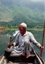 INDIA, Kashmir, Srinagar, Nagin Lake. Man sitting in boat smoking a Hookah pipe