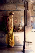 INDIA, Rajasthan, Mt Abu, Fly monk standing near Buddha statues with a scarf covering his head and