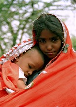 INDIA, Rajasthan, Pushkar, Portrait of a young girl wrapped in a red shawl with her younger brother