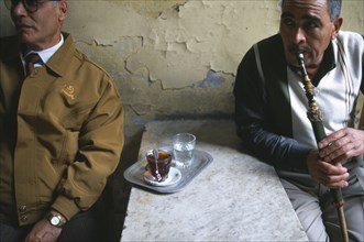 EGYPT, Nile Delta, Alexandria, Two men in street cafe one drinking tea and one smoking a sheesha