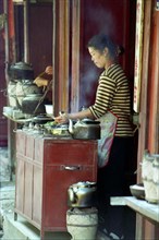 CHINA, Yunnan, Lijiang, Female vendor at a street stall cooking and serving tea