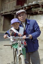 CHINA, Yunnan, Lijiang, Portrait of a man standing with a small boy on his bike holding a Pepsi