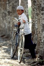 CHINA, Gansu, Linxia, Boy standing with an adults bike in a tree lined street