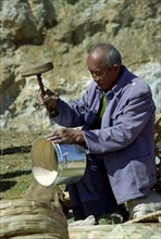 CHINA, Yunnan, Shapin, Man using old style drilling tool on metal and wooden pot