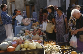 FRANCE, Midi Pyrenees, Caussade, Man with customers selling gourds at weekly market stall