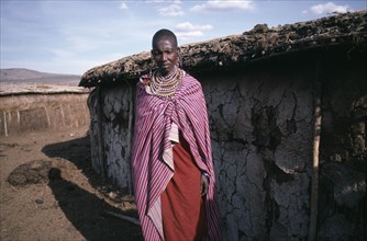 KENYA, Tribal People, Masai woman standing outside traditional mud dwelling near the Masai Mara.