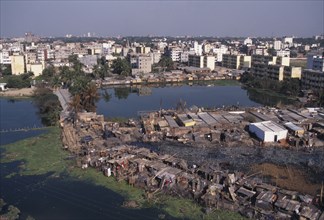 BANGLADESH, Dhaka, Waterside slum dwellings after fire with city buildings beyond.