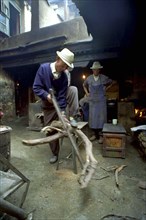 CHINA, Tibet, Lhasa, Elderly man cutting firewood for the kitchen in a courtyard