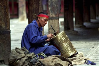 CHINA, Tibet, Lhasa, Man repairing prayer wheel as Penance at the Jokhang Temple