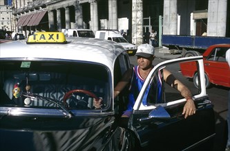 CUBA, Havana, Driver standing by the open door of his classic American style black cab parked