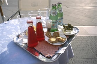 ITALY, Trieste, Piazza Unita, Tray on a small round lace clothed table with glasses and two bottles