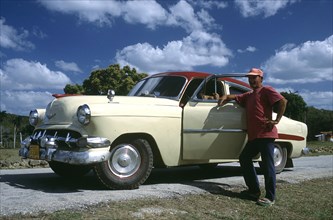 CUBA, Cienfuegos, Man standing by the open door of a classic style American car which has been