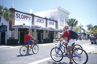 USA, Florida, Key West, Cyclists on Duval Street outside Sloppy Joes Bar