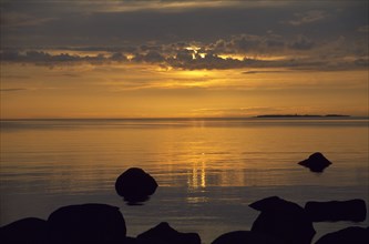ESTONIA, Sunset, Sunset over water with rocks in the foreground on the longest day of the year