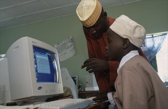 NIGERIA, Education, Teacher leaning over boy sitting at a computer in a classroom