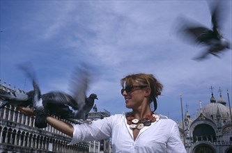 ITALY, Veneto, Venice, St Marks Square. Woman wearing a white shirt standing with pigeons