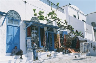 TUNISIA, Sidi Bou Said, Rugs and postcards for sale.  White painted shopfront with blue doors.  Two