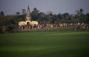 BANGLADESH, Aricha, View over rice fields towards crowds gathered around old Hindu temple at sunset
